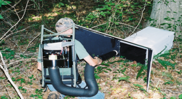 Mosquito resting box Person handling mosquito surveillance equipment placed on the ground in a wooded area.