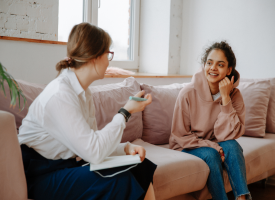 Untitled design - 1 Teen girl looking happy while sitting on a couch speaking with a therapist