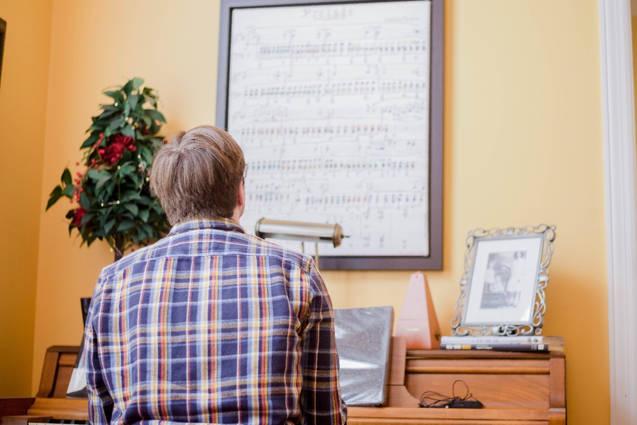 Ben looks up at a painting of song chords painted as piano sheet music that hands above his antique piano