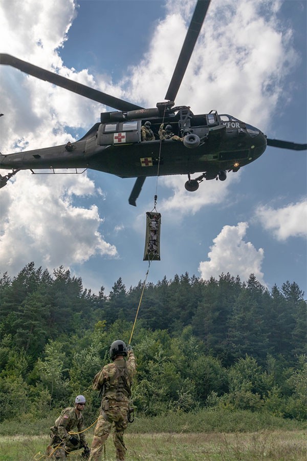 Soldiers from the Tennessee National Guard and a helicopter in the air during training at a wooded area in Kosovo.