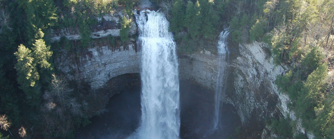 A large waterfalls pours over a high cliff
