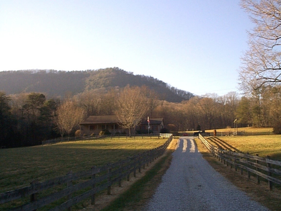 A gravel road flanked by wooden fences leads to a rustic building