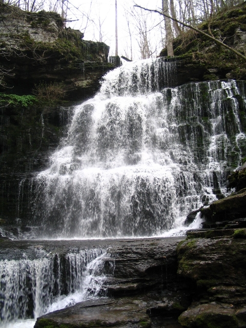 A medium-sized waterfall cascades over three tiers of stone into a river
